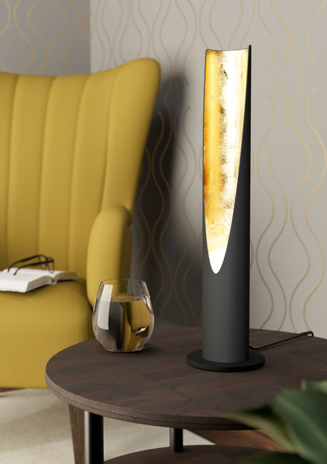 EGLO Barbotto 97583 encendida sobre una mesa junto a un sillón, acabado negro y dorado